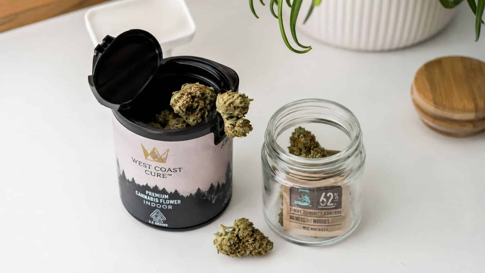 A container of West Coast Cure cannabis flower and a humidity control pack inside a glass jar.